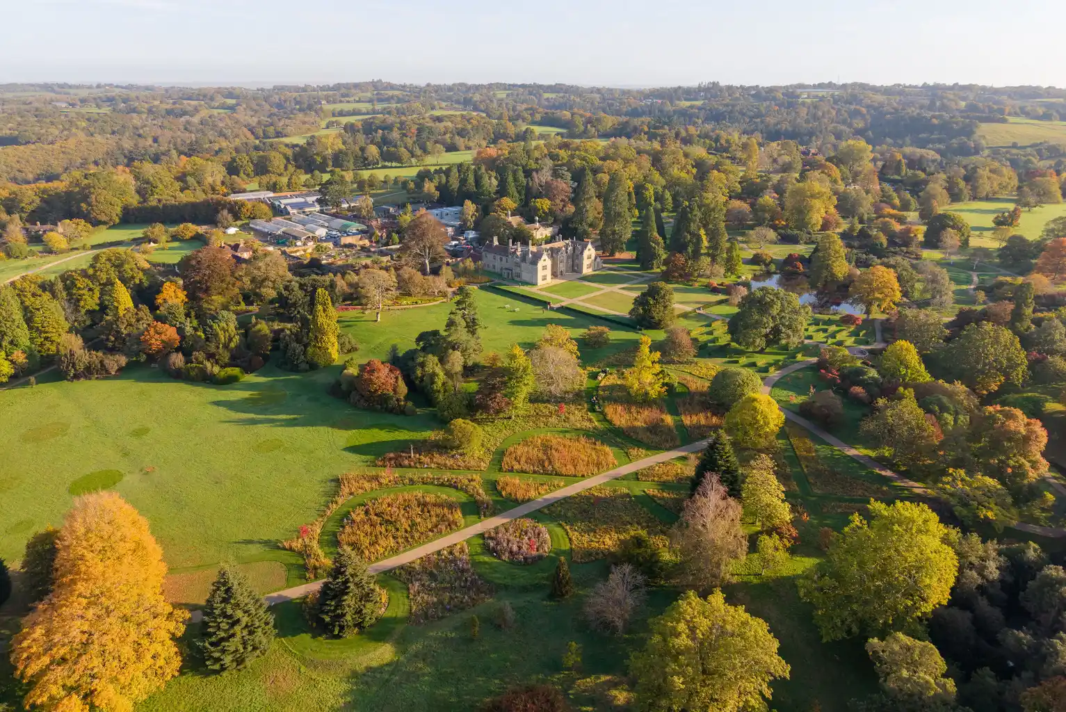 Aerial view of Kew Wakehurst’s gardens and mansion surrounded by autumn trees