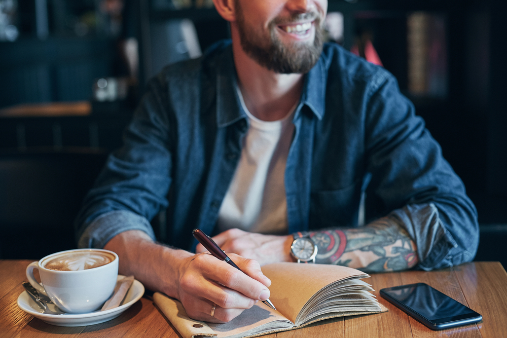 Man writing ideas in a notebook while recognising opportunities in everyday life