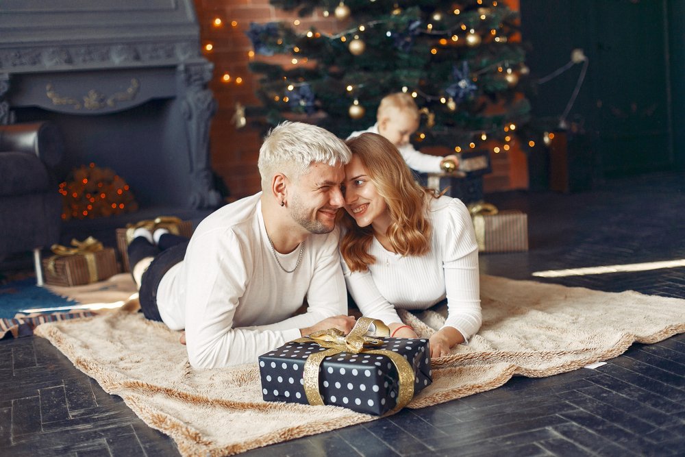 Christmas gift ideas for the family: parents with a wrapped present beside a Christmas tree