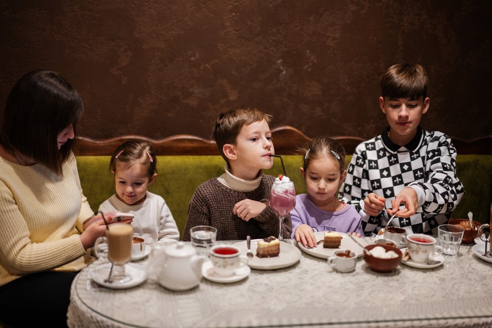A mother and four children enjoying drinks and desserts together in a café